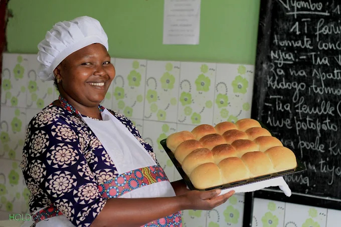 Teen mom learning culinary arts in chef hat holding a tray of buns.