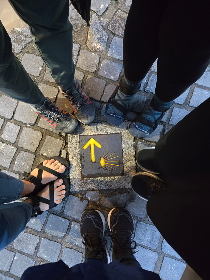 A circle of women, view of their feet surrounding a plaque on cobblestone.