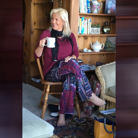 Cindy Bohnett with a cup in her hand sitting cross legged.