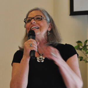 Karen standing with a microphone and wearing glasses.