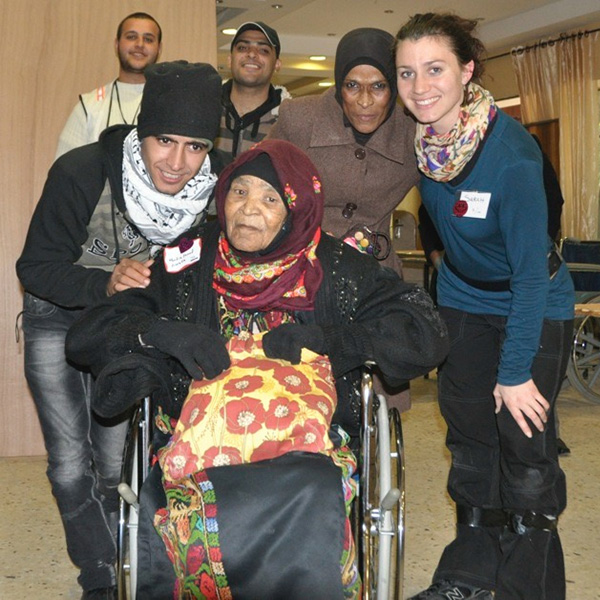 An older woman sitting in a wheelchair surrounded by volunteers - all smiling.
