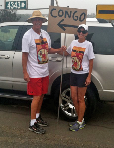 Fellow cyclists holding a sign that says Congo with an arrow pointing left - wearing the Ride and Shine 500 t-shirts.