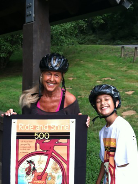 Anastasia holding the Ride and Shine 500 poster standing with her grandson w- both training for the event.