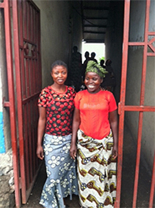 Two smiling women standing in a hall leafing outside in Rwanda.